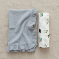 Blue ruffled baby blanket and a folded woodland swaddle on a beige surface