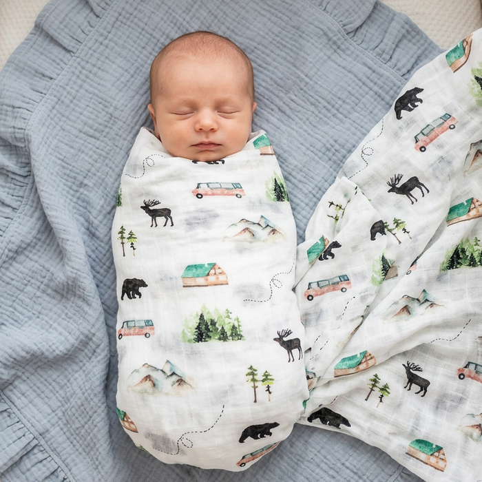 Newborn baby swaddled in a woodland blanket on a blue muslin blanket