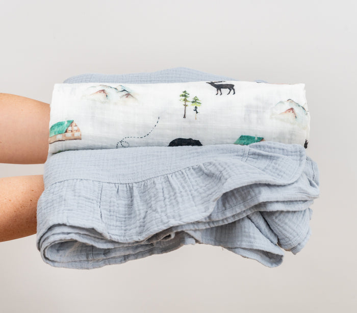 Stacked baby blanket with with woodland swaddle rolled on top.