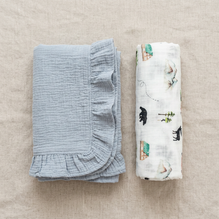 Folded light blue baby blanket with woodland printed swaddle on a beige surface
