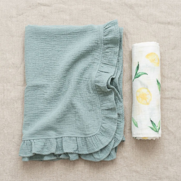 muslin green ruffled blanket and white swaddle with lemon design on a beige surface