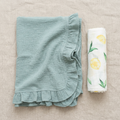 muslin green ruffled blanket and white swaddle with lemon design on a beige surface