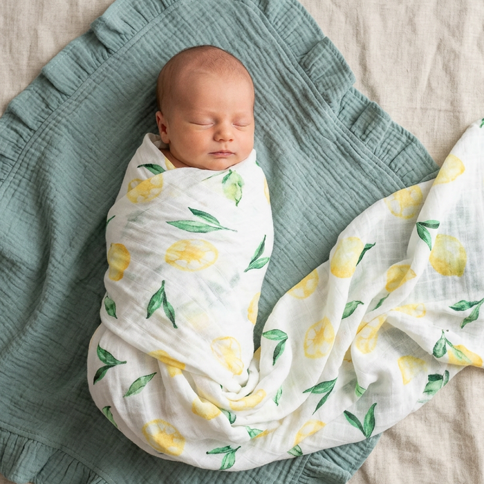 Newborn baby swaddled in a lemon-patterned swaddle on a green muslin blanket