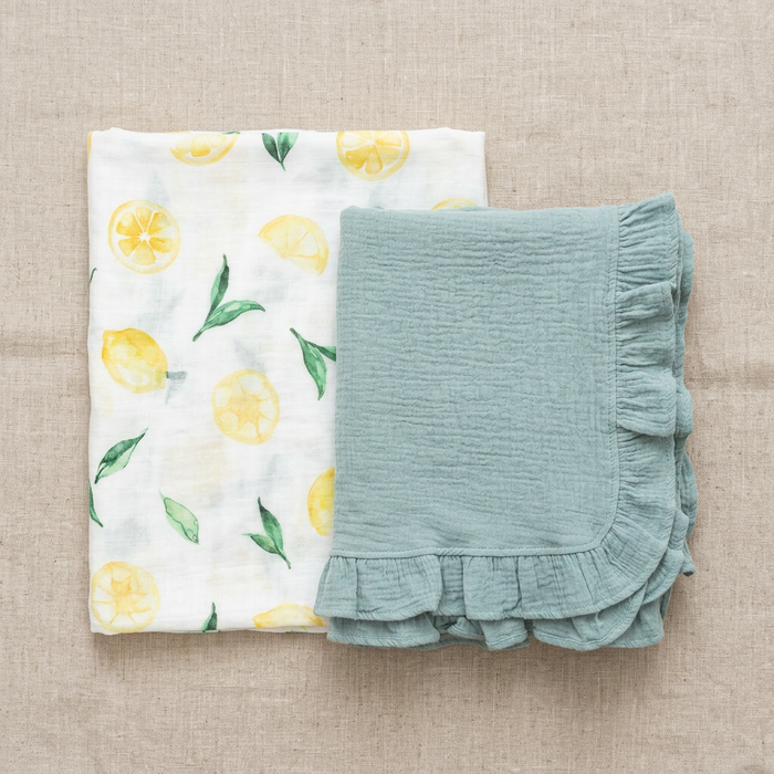 Muslin swaddle and baby blanket, one with lemon pattern and the other with ruffled edge, on a beige fabric background.