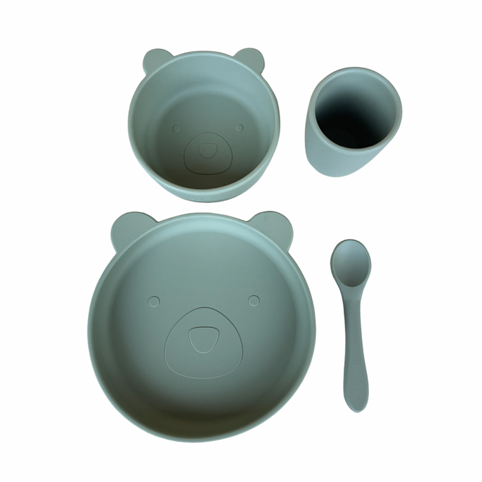 A four-piece baby and toddler dinnerware set in sage green, including a suction plate, suction bowl, spoon, and cup, each with a bear face design.