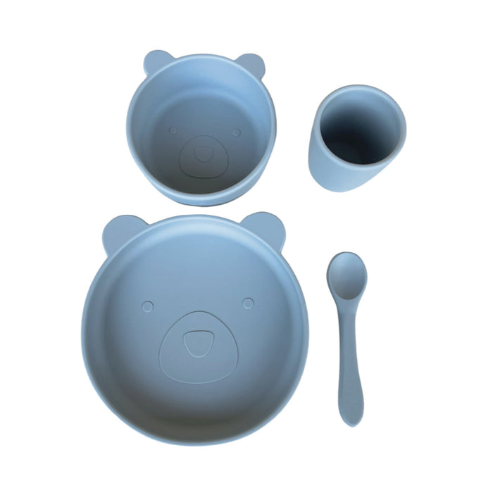 A four-piece baby and toddler dinnerware set in blue, including a suction plate, suction bowl, spoon, and cup, each with a bear face design.