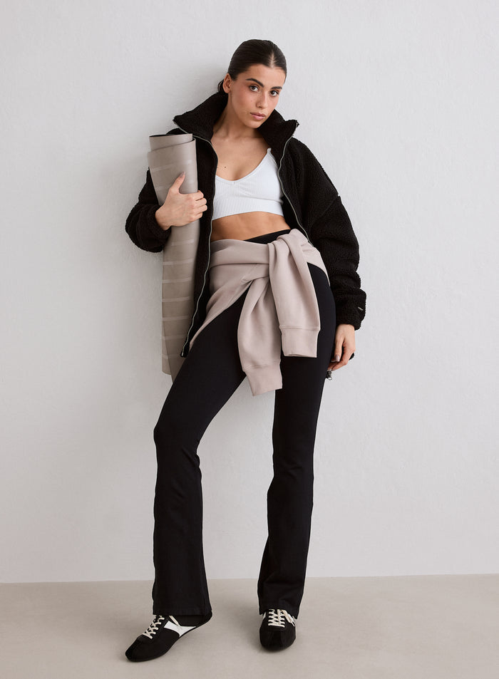 Nainen yllään musta Pile Jacket, valkoinen urheilutoppi ja mustat trikoot pitelemässä joogamattoa. [M-174cm]