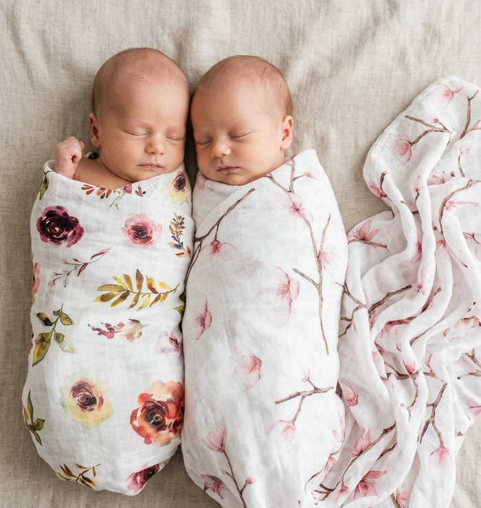 Two babies swaddled in floral blankets on a beige surface