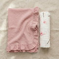 Pink ruffled blanket and floral-patterned swaddle on a textured surface