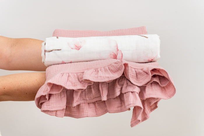 Stacked flocked muslin swaddle and pink baby blanket held by a person against a light background