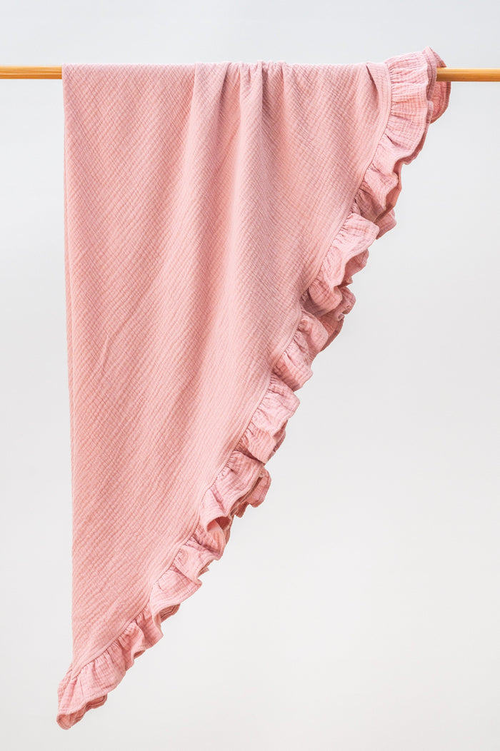 Blush pink heirloom ruffle muslin baby blanket folded neatly, featuring lightweight organic muslin and a gentle ruffle edge.