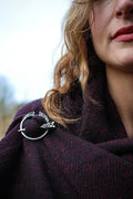 Close up of silver plated Celtic penannular brooch with Trinity knot detail fastening a burgundy shawl