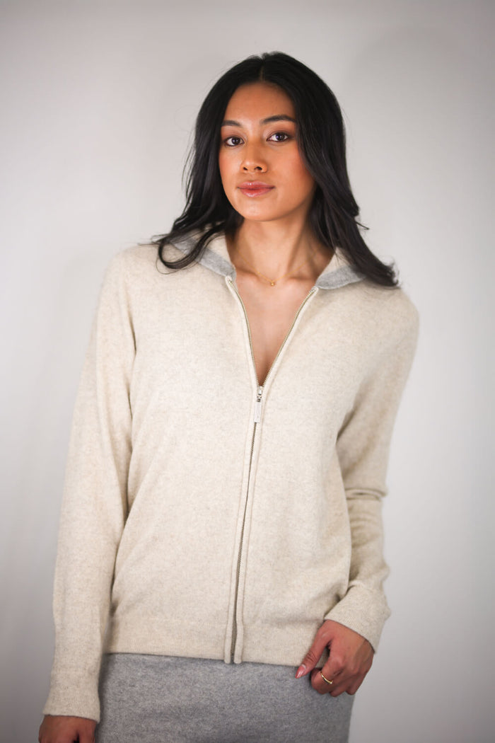 Woman wearing a beige zip-up hoodie against a plain background
