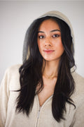 Woman wearing a beige hoodie with long dark hair against a plain background