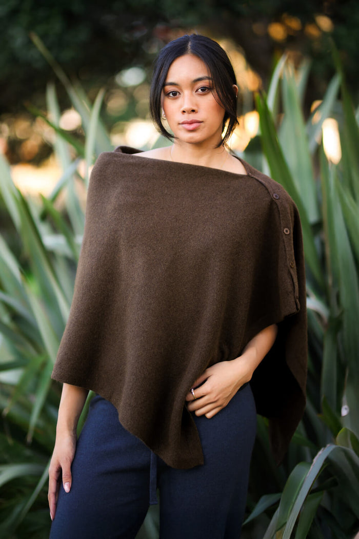 Woman wearing a brown poncho standing among green plants