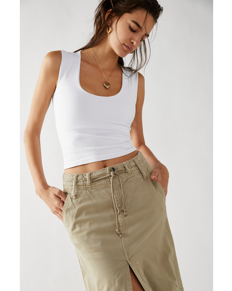 A female model wearing a white scoop-neck sleeveless tank top paired with a beige skirt.