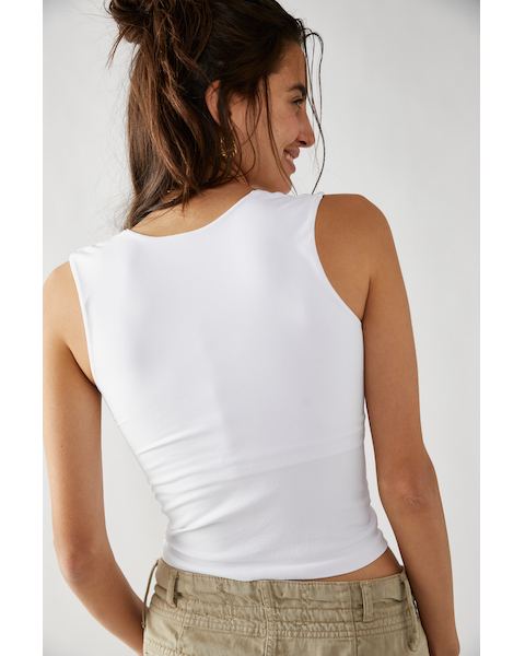 A female model wearing a white scoop-neck sleeveless tank top paired with a beige skirt, back view