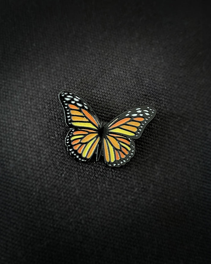 Ela Mo™ Mini Pin für Rucksäcke | Butterfly. Ein kleiner Schmetterlings-Pin auf dem schwarzen Rucksack befestigt.