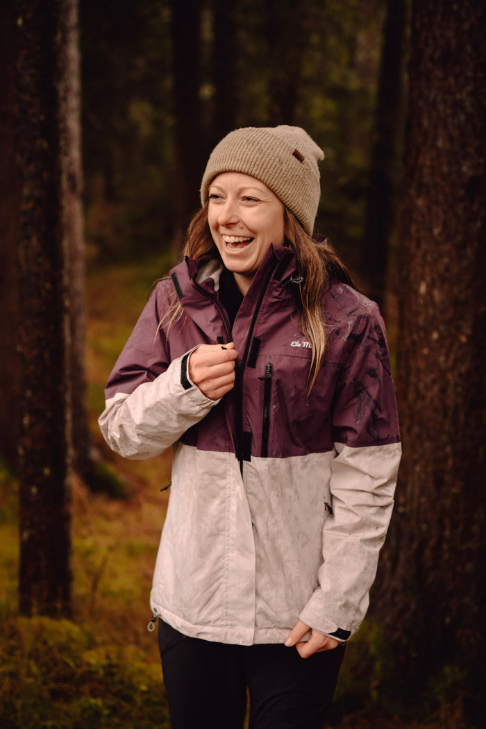 Ela Mo™ Regenjacke | Grape. Eine Frau im regnerischen Wald mit einer Regenjacke.