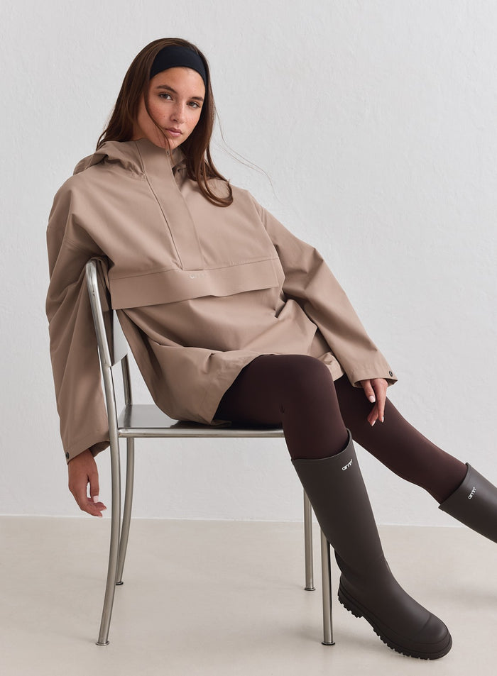 Malli, jolla on päällään Espresso Waterproof Oversized Anorak, istumassa tuolilla [M-178cm]
