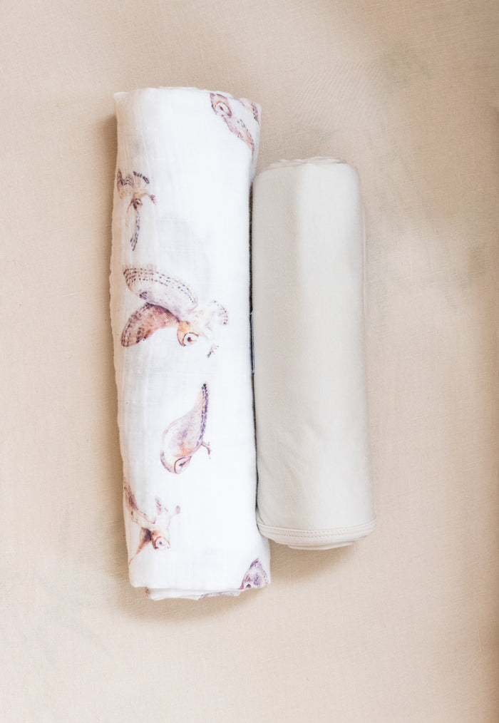 Two rolled-up swaddles, one with an owl pattern and the other neutral, on a beige background.