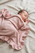 Newborn baby wrapped in a blush heirloom muslin blanket on a light surface