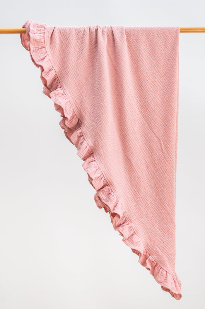Blush pink heirloom ruffle muslin baby blanket folded neatly, featuring lightweight organic muslin and a gentle ruffle edge.