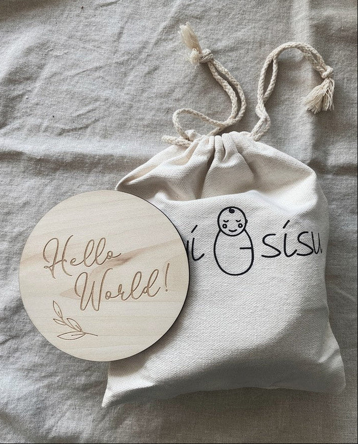 Milestone cards. Wooden 'Hello World!' disc with a drawstring bag on a textured fabric background