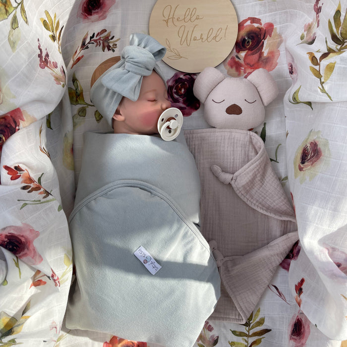 Newborn baby wrapped in floral muslin swaddle with organic muslin koala baby and toddler comforter