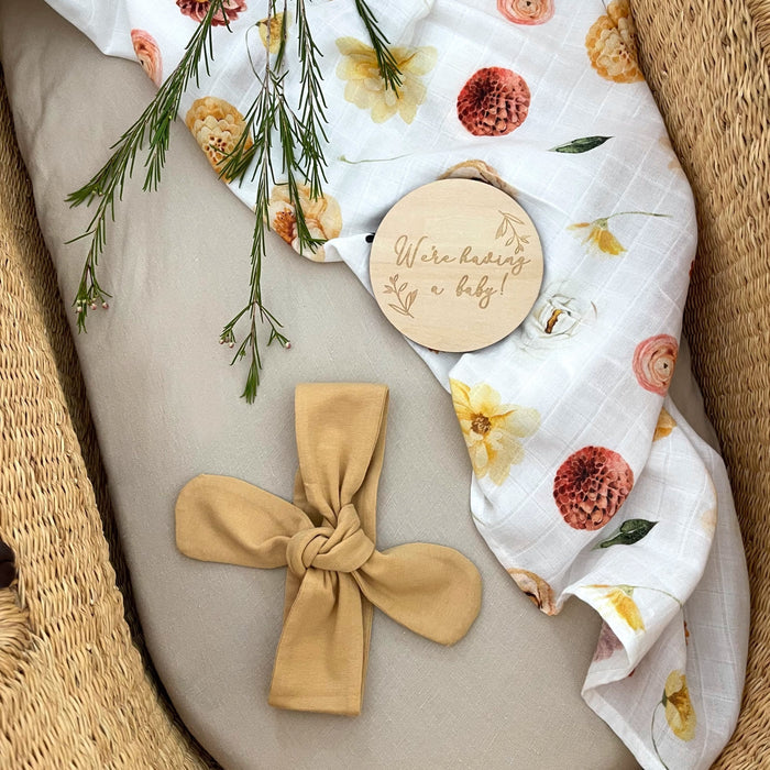 Pregnancy announcement milestone card 'We're having a baby' with headband and organic muslin swaddle.