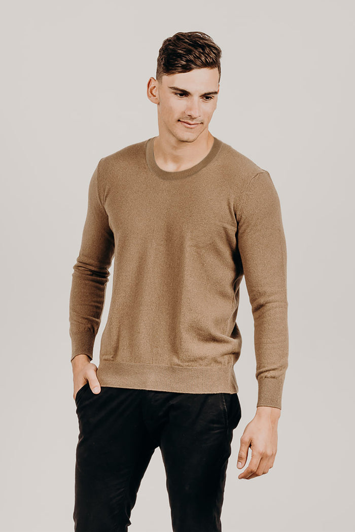 Man wearing a brown sweater and black pants against a plain background