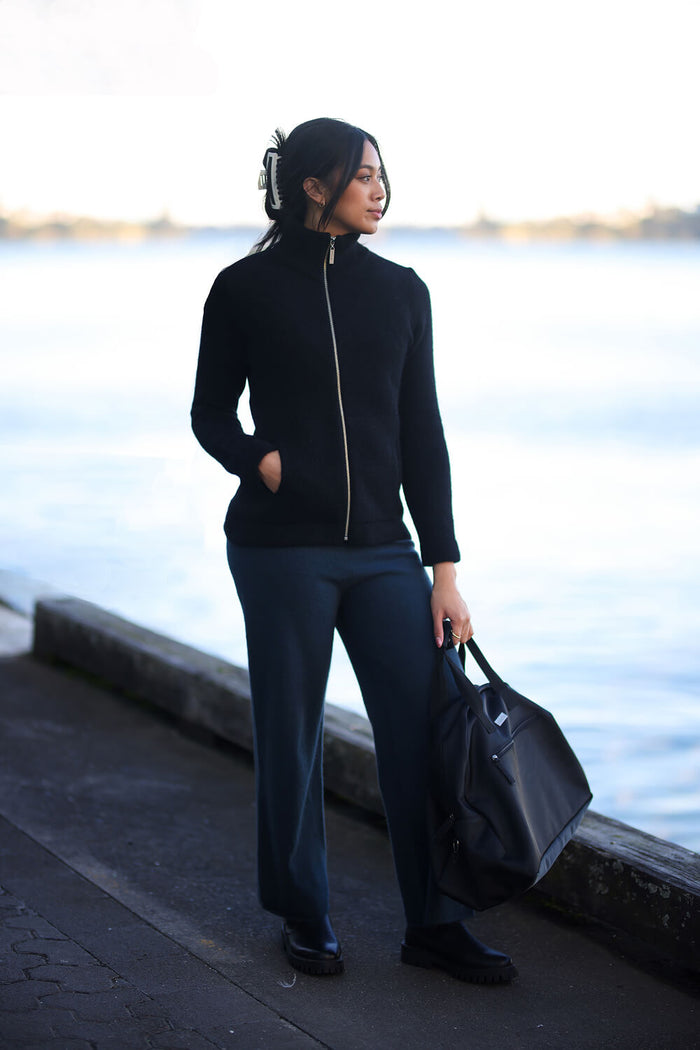 Woman in black outfit holding a black bag by a waterfront