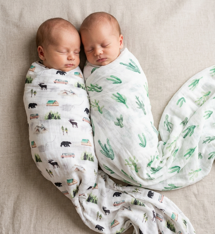 Two babies swaddled in patterned swaddles on a beige surface