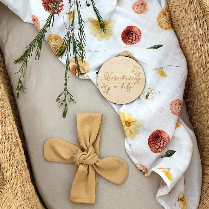Pregnancy announcement milestone card 'We're having a baby' with headband and organic muslin swaddle.