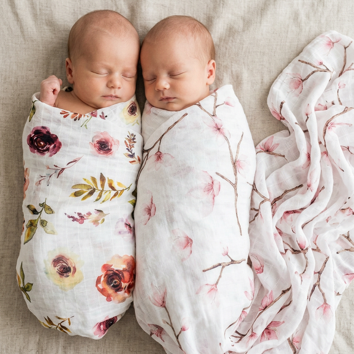 Two babies swaddled in floral blankets on a beige surface