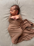 Newborn baby swaddled in a chocolate brown jersey wrap on a linen surface