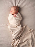 Newborn baby wrapped in an organic jersey swaddle with matching beanie in Fog, creating a calm and soothing newborn moment.