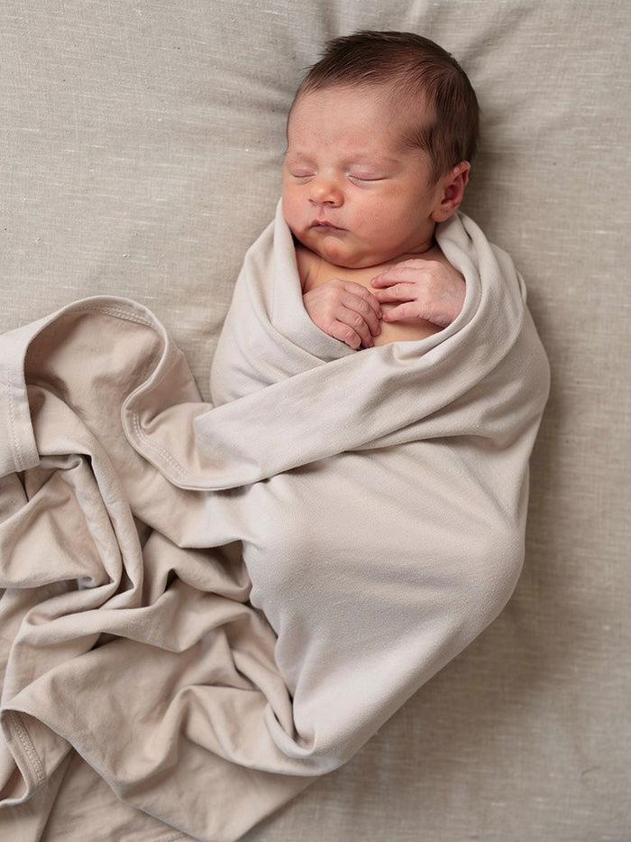 Lifestyle image of a newborn peacefully swaddled in the Fog organic jersey swaddle with matching beanie.