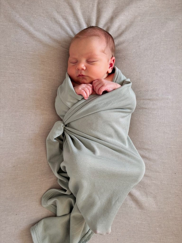 Newborn baby wrapped in an organic jersey swaddle in Mineral, creating a calm and cosy newborn moment.