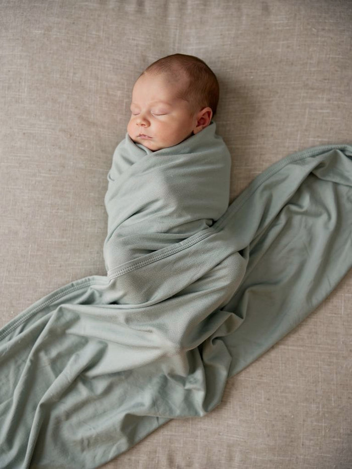 Lifestyle image of a newborn peacefully swaddled in the Mineral organic jersey swaddle.