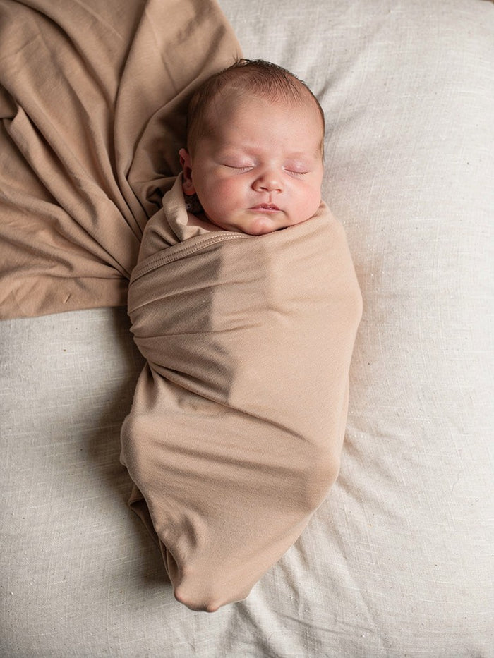 Newborn baby wrapped in a sand swaddle on a soft surface