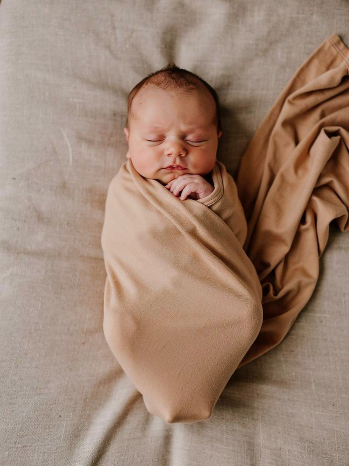Newborn baby wrapped in a organic jersey swaddle wrap on a soft surface
