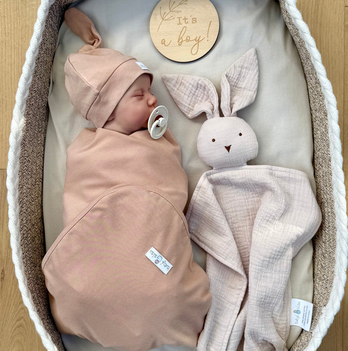 Gender reveal. Newborn baby swaddled in a moses basket with a bunny comforter and milestone card 'it's a boy'