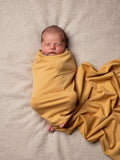 Newborn baby wrapped in an organic jersey swaddle with matching beanie in Turmeric, creating a warm and comforting newborn moment.