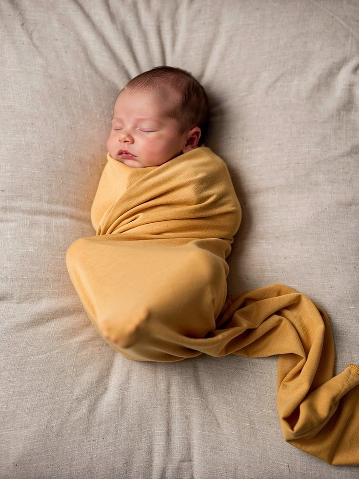 Lifestyle image of a newborn peacefully swaddled in the Turmeric organic jersey swaddle.