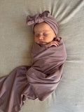 Newborn baby wrapped in an organic jersey swaddle with matching topknot in Amethyst, creating a calm and comforting newborn moment.