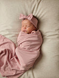 Newborn baby wrapped in an organic jersey swaddle with matching topknot in Rose Quartz, creating a soft and soothing newborn moment.