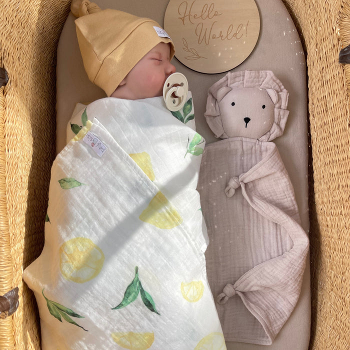 Baby wrapped in a lemon-patterned swaddle with organic muslin Lion comforter with knotted corners