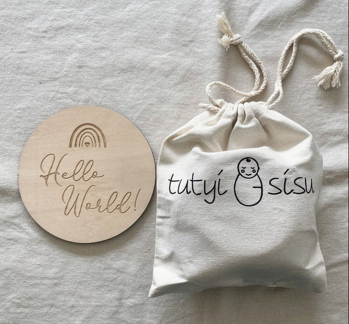 Milestone cards with keepsake pouch. Round wooden disc with rainbow and  'Hello World!' text on a light gray fabric background.
