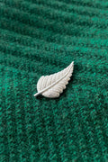 Silver leaf-shaped brooch on a green textured fabric background